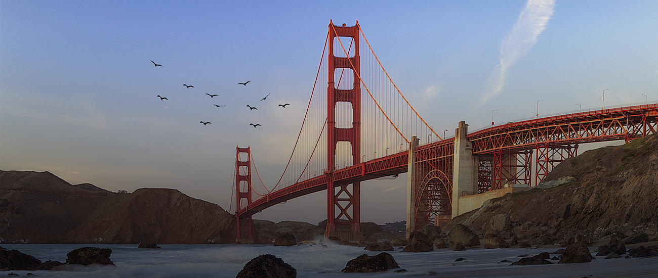 The Golden Gate Bridge at dusk with birds flying in the sky above.